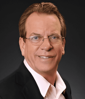 Man in glasses wearing a suit, smiling.