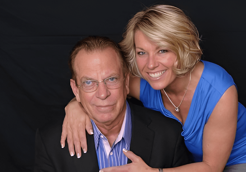 ae8f470c94976e6b61dc838a15e166cc-Picsart-AiImageEnhancer Smiling woman embracing seated man, black background.